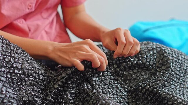 Detailed shot of hands pressing and popping black bubble wrap as satisfying sensory activity