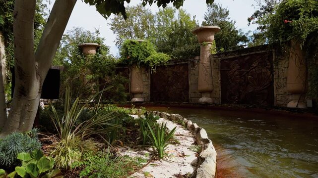 Themed columns and carved walls line a curved water channel at Gardaland in Italy. Trees and plants surround the Fuga da Atlantide ride.