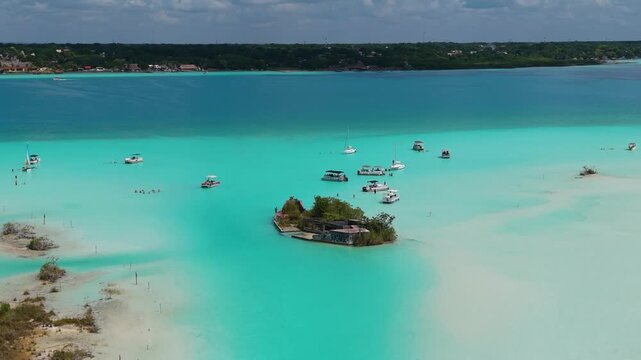 Several small watercraft float across crystal-clear aquamarine shallows and sandy shoals.