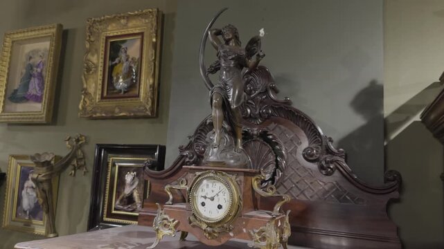 Close up of an ornate antique bronze mantel clock decorated with a figural sculpture surrounded by gilded picture frames in a vintage collection