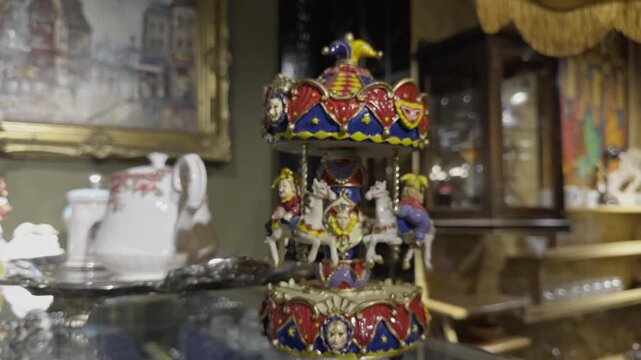 Detailed close up view of a decorative carousel music box featuring painted horses and jester riders on an antique display shelf