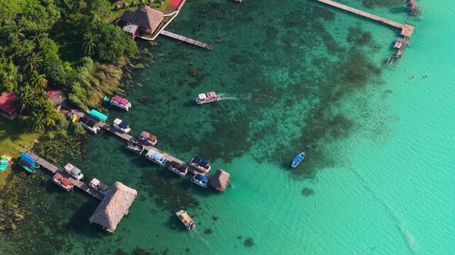 Small watercraft tie up at thatched-roof piers extending across bright aquamarine shallows.
