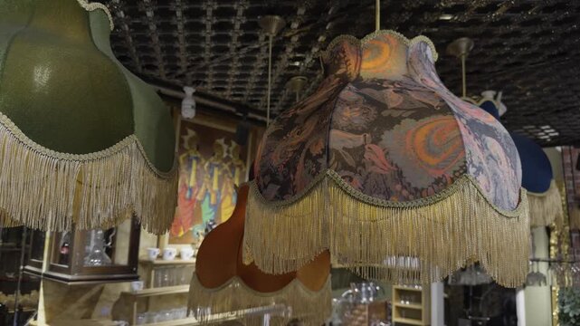 Close view of a paisley patterned fringe lampshade next to a green velvet shade hanging in a colorful vintage lighting shop