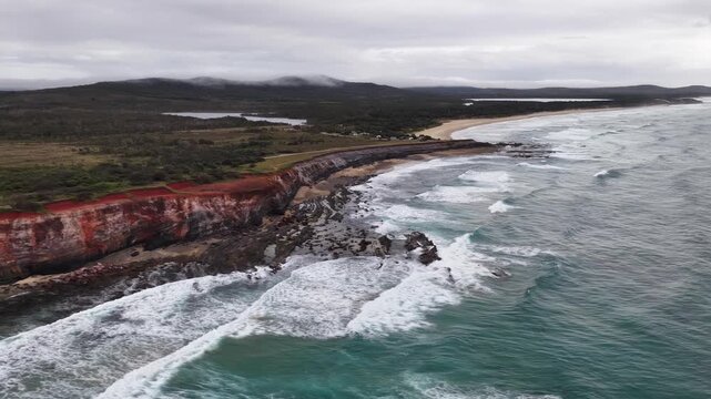 Aerial video flying over the rugged coastline at Lake Arragan, featuring sandy shoreline, rocky formations and waves rolling in from the Pacific Ocean