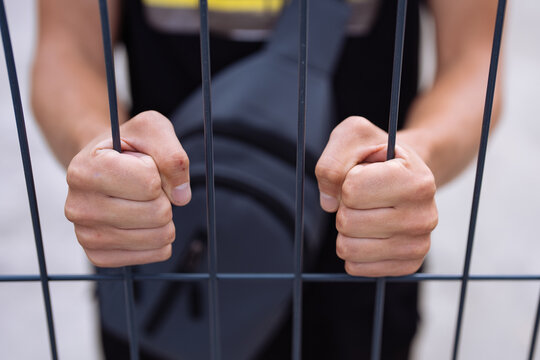 A powerful and emotional close-up shot of a person's hands tightly gripping a metal wire fence. Concepts of captivity, confinement, restriction, and the desperate desire for freedom or escape.