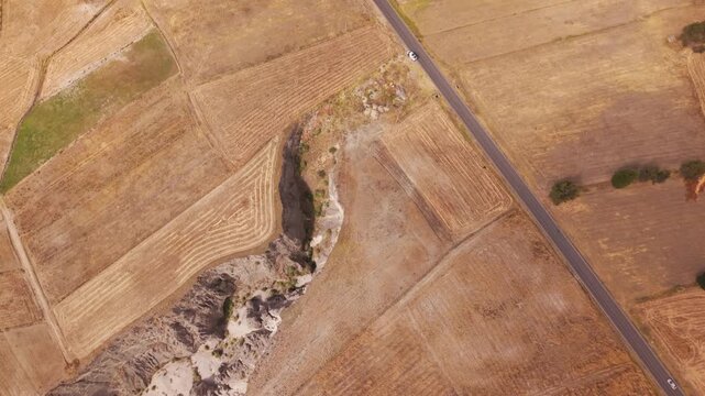 Top down aerial view of a car driving along a road next to dry fields and the toacachi canyon