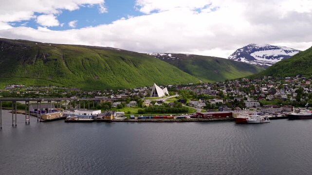 Tromso Arctic Cathedral Bridge waterfront buildings and surrounding mountains beside the Tromsoysundet strait in summer, aerial dolly forward