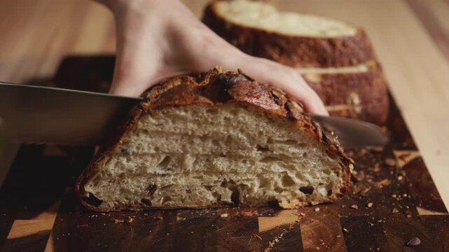 Close-up of hands slicing freshly baked artisan sourdough bread with a knife on a wooden cutting board. Homemade crusty open crumb loaf for breakfast, bakery promos, and healthy food concepts.