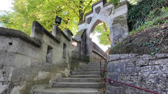 Slow motion ascent along a stone staircase beneath a Gothic arch at Pierrefonds Castle, surrounded by weathered walls, moss and autumn foliage