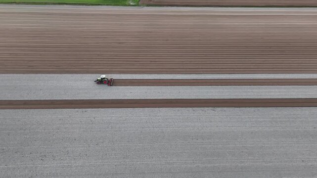 A tractor works between broad parallel cultivated plots, creating a strong geometric pattern of agricultural land and contrasting soil textures across the intensively farmed plain.