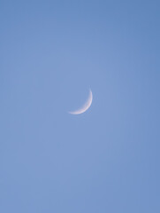 Bright young crescent moon glowing softly in a clear blue daytime sky. Minimalist astronomical background featuring a thin waxing moon phase in a calm atmosphere during early evening or late afternoon © Muhammad