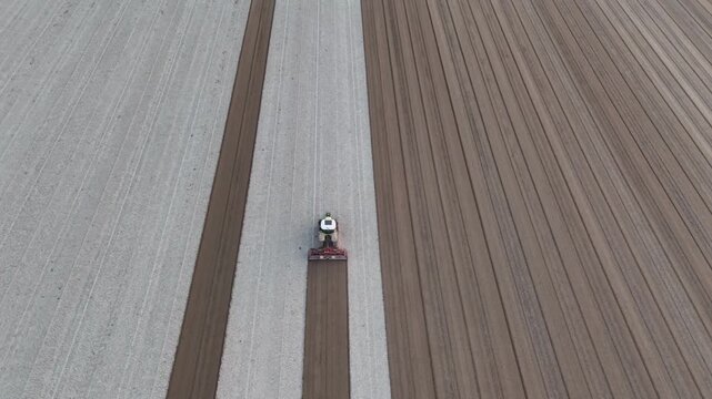 Tractor performs secondary tillage across freshly ploughed soil, breaking clods and leveling surface to prepare uniform seedbed in Po Valley, Emilia Romagna, Italy, drone tracking slow motion.