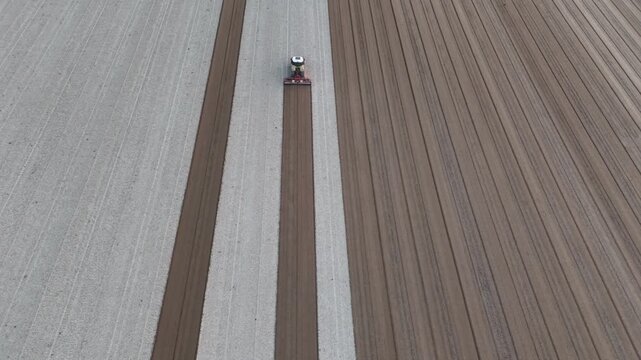 A tractor pulls a tillage implement through freshly ploughed ground, breaking soil clods and conditioning the surface into a more uniform seedbed while following long parallel agricultural strips.