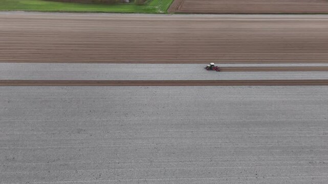 A tractor performs secondary tillage across freshly ploughed soil, breaking clods and conditioning the surface into a uniform seedbed in the Po Valley of Emilia Romagna, drone tracking.