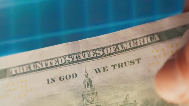 A close-up shows a hand holding a hundred dollar bill against a blue stock market graph. This visual is ideal for financial reports, investment concepts, and economic projects.