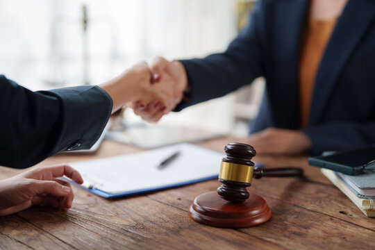 Lawyers or business people shaking hands, sealing a legal deal or partnership agreement, with a gavel and documents on the desk representing justice and law