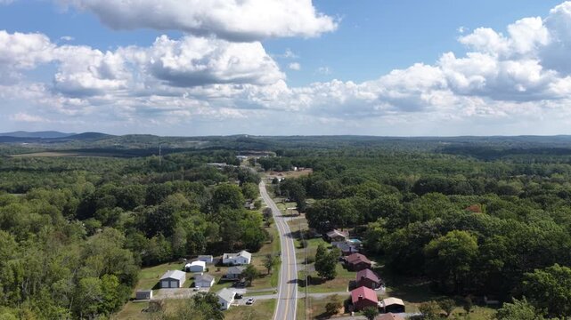 A two lane highway threads through wooded countryside outside Lynchburg, Virginia, scattered houses along the verge and rolling forest running back to the horizon. Aerial forward wide shot