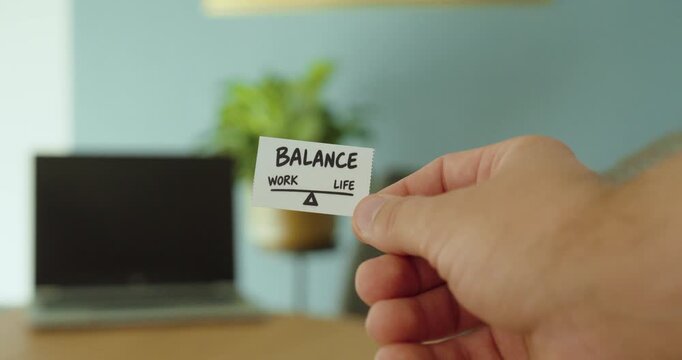 Close-up of hand holding a work life balance card, representing healthy boundaries, wellbeing and balance between career and personal life.
