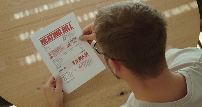 Shocked man reacting to an extremely high heating bill, worried about rising energy costs and household expenses.