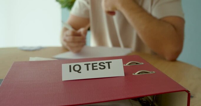 Person taking an IQ test at a desk, writing answers on paper with an IQ Test sign in the foreground.