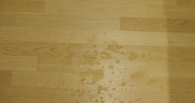 Close-up of spilled water splashing and spreading across a wooden parquet floor.