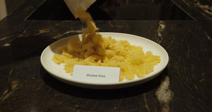 Gluten-free pasta being poured onto a plate beside a visible label, representing special diets, food intolerance and healthy eating choices.