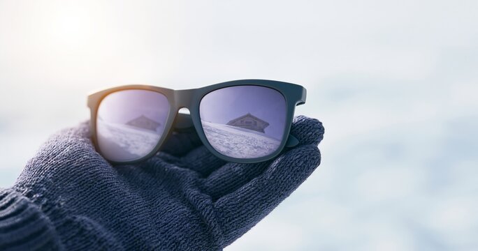 Winter sunglasses reflecting snowy cabin scene