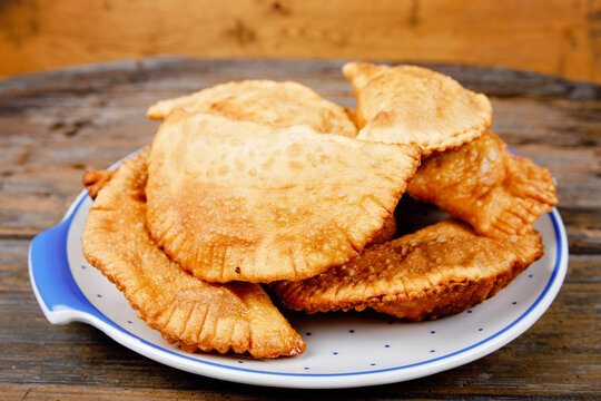 Homemade chebureks filled with minced meat and onions, traditional Caucasian and Russian cuisine. Close-up of group of fresh fried meat pastry pie called cheburek on wooden table.