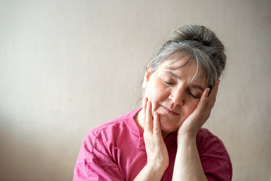 Middle aged woman resting her face in her hands indoors with closed eyes. Menopause awareness hot flashes perimenopause fatigue and women's health