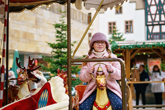 Little school girl riding on a merry go round carousel at Christmas funfair or market, outdoors. Happy child having fun on traditional family xmas market in Germany
