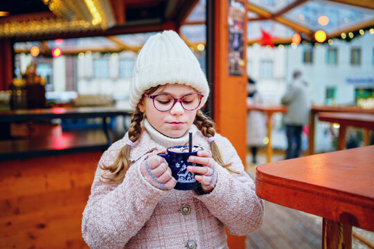 Little cute preschool girl drinking hot children punch or chocolate on German Christmas market. Happy child on traditional family market in Germany,