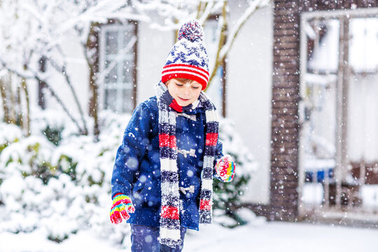Cute little funny child in colorful winter fashion clothes having fun and playing with snow, outdoors during snowfall. Active outdoors leisure with children. Kid boy and toddler catching snowflakes.