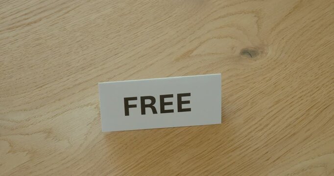 Close-up of hand placing a Free sign on a wooden table