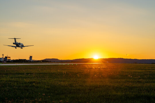 Business jet landing over an airfield control tower at sunset