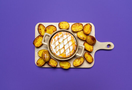 Baked camembert with roasted potatoes on a purple background