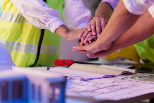 Engineers and architects stacking hands over blueprint for construction teamwork