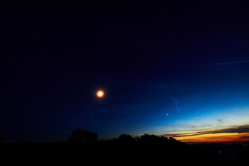Moon on a twilight sky with stars, planets and landscape mountain silhouettes. © astrosystem