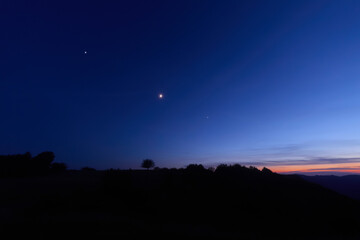 Moon on a twilight sky with stars, planets and landscape mountain silhouettes. © astrosystem