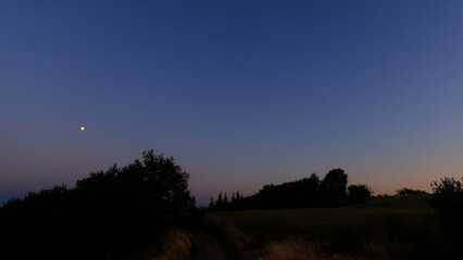 Moon on a twilight sky with stars, planets and landscape mountain silhouettes. © astrosystem
