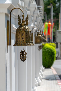 Ornate brass temple bell hanging white wall, peaceful street scene
