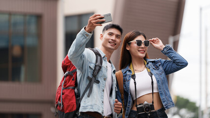 Obraz premium Happy Asian couple taking selfie with smartphone while traveling in city