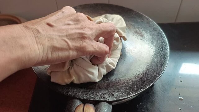 Indian woman pressing and puffing flatbread roti on iron tawa with cloth close up
