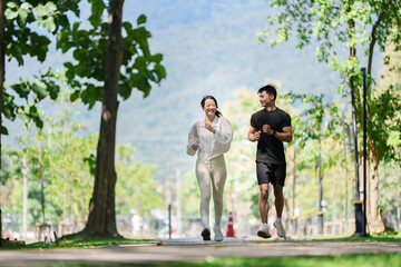 Fototapeta premium Smiling Asian couple jogging together in park for outdoor cardio workout