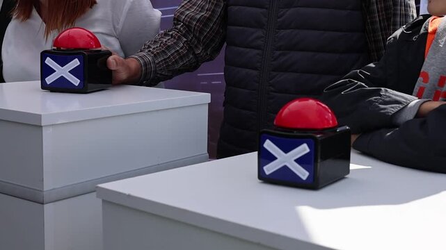 Hand pressing a large red buzzer button on a white podium during a game show or quiz event