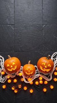three carved halloween pumpkins with smiling faces and orange string lights on dark slate background halloween decoration concept