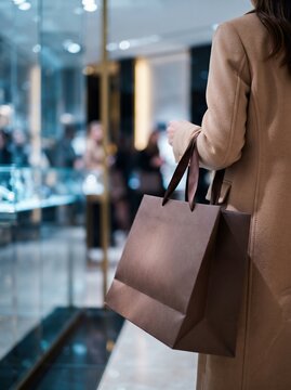 Shopping woman carrying brown paper bag walking in high-end retail store, luxury consumerism experience.