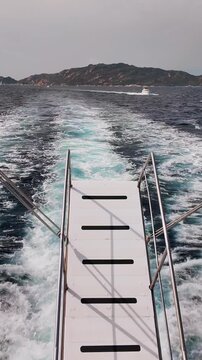 Vertical view from the stern of a motorboat speeding across a rough, dark blue sea, leaving behind a wide, dynamic wake of white, foaming water.