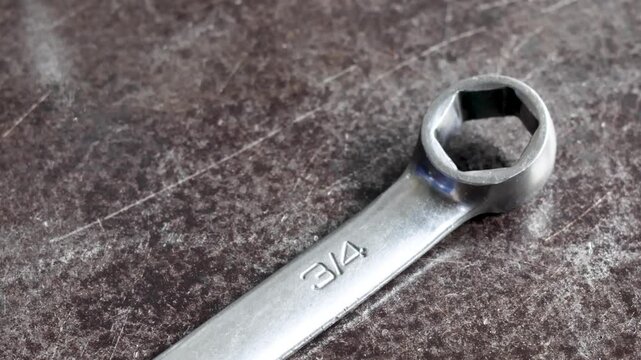 Panning shot of metallic box end spanner wrench resting on workshop workbench.