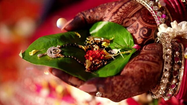 A close-up, high-angle shot of a bride holding manga sutra cupped together holding a vibrant green betel leaf, adorned with intricate dark brown henna patterns