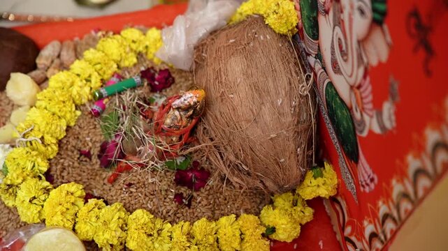 A close-up, high-angle shot of a traditional Hindu puja setup, featuring a whole coconut wrapped in red thread